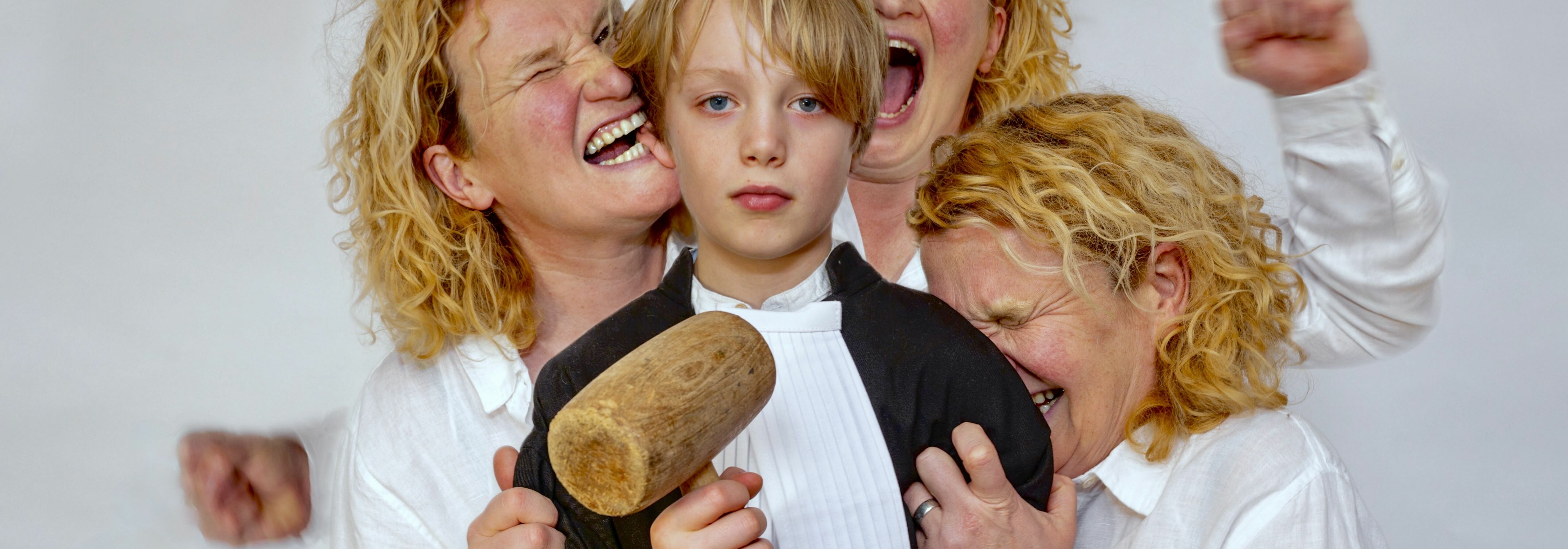 Afbeelding van de voorstelling: Een vrouw zit op een stoel in een rechtszaal en kijkt naar beneden, een blond jongetje legt zijn hand op haar schouder en draagt advocatenkleding.