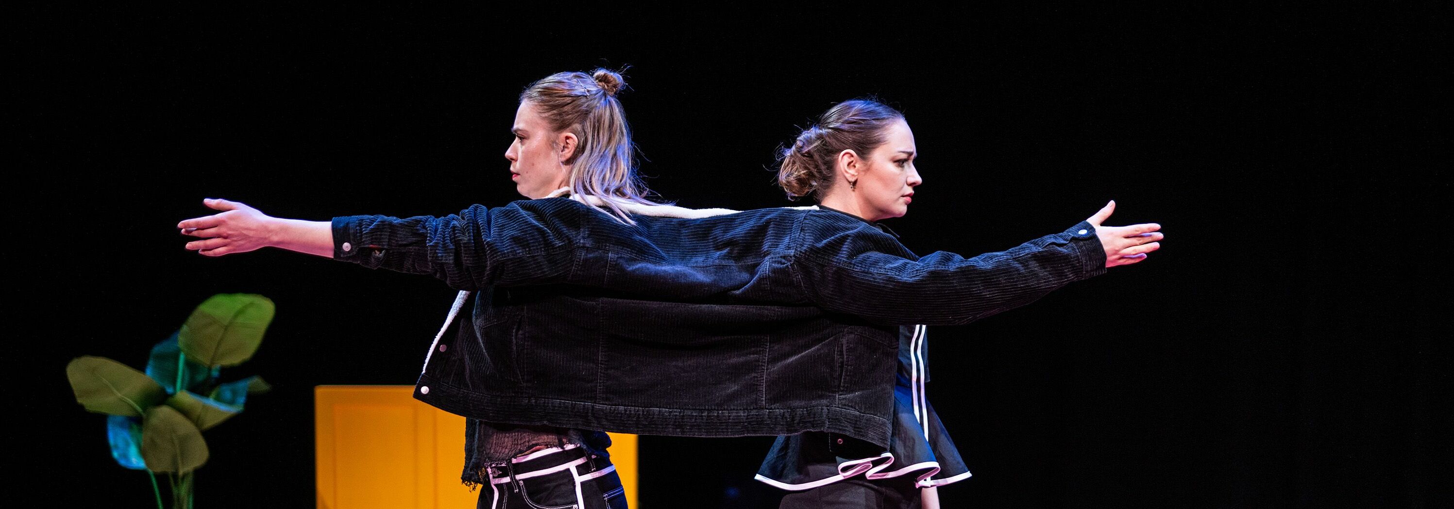Afbeelding van de voorstelling: Vier personen staan geposeerd voor een groot huis in een tuin. Ze bewegen met hun armen in verschillende directies en kijken elk een andere kant op.