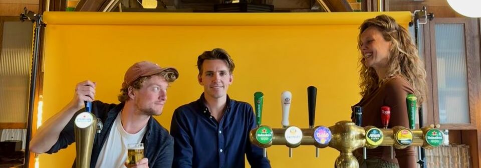 Afbeelding van de voorstelling: Twee personen staat richting publiek, de vrouw spreekt door de microfoon en de man rechts luistert aandachtig. De omgeving lijkt een soort café te zijn.